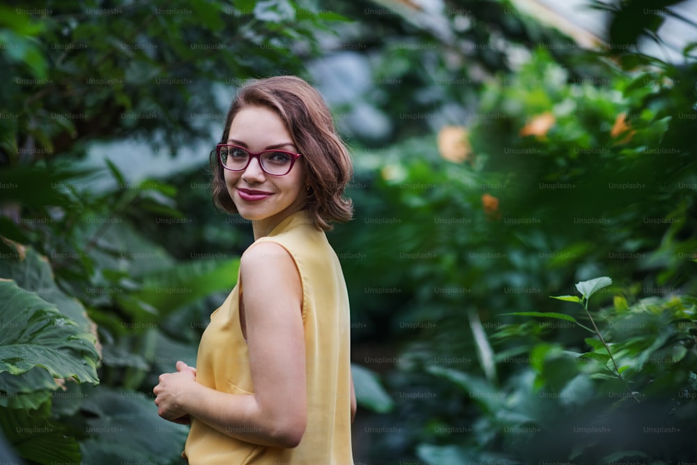 A young woman standing in botanical garden, looking at camera. Copy space.