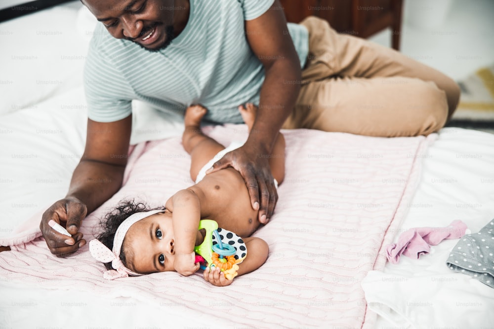 Süßes afroamerikanisches Mädchen, das auf dem Bett liegt, während der lächelnde Papa die Hand auf ihr Bauch-Stockfoto legt