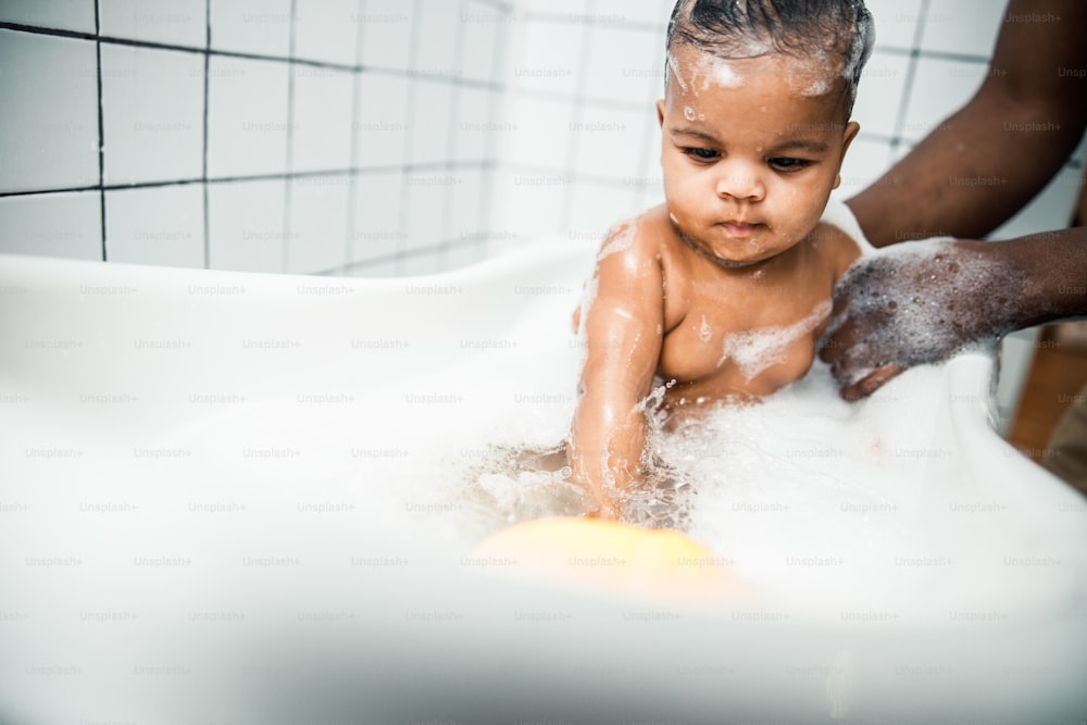 Gros plan de mains masculines afro-américaines baignant un mignon nouveau-né dans une baignoire avec une photo de stock. Bannière de site web