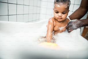Close up of Afro American male hands bathing cute newborn child in bathtub with foam stock photo. Website banner