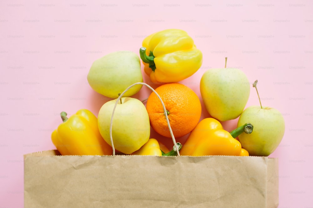 Obst und Gemüse in Papiertüte auf rosa Hintergrund flach legen. Zero Waste Shopping, plastikfrei. Lebensmittel online einkaufen. Bestellen Sie frische Bio-Lebensmittel und lassen Sie sie sicher liefern.