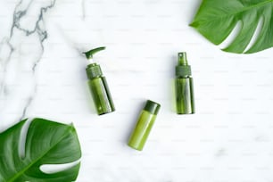 Frascos cosméticos verdes con hojas de plantas tropicales monstera sobre fondo de mármol. Productos cosméticos SPA orgánicos naturales, cuidado de la piel y concepto de tratamiento de belleza
