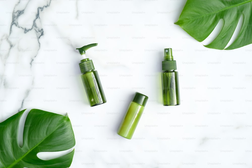 Green cosmetic bottles with monstera tropical plant leaves on marble background. Natural organic SPA cosmetic products, skincare and beauty treatment concept