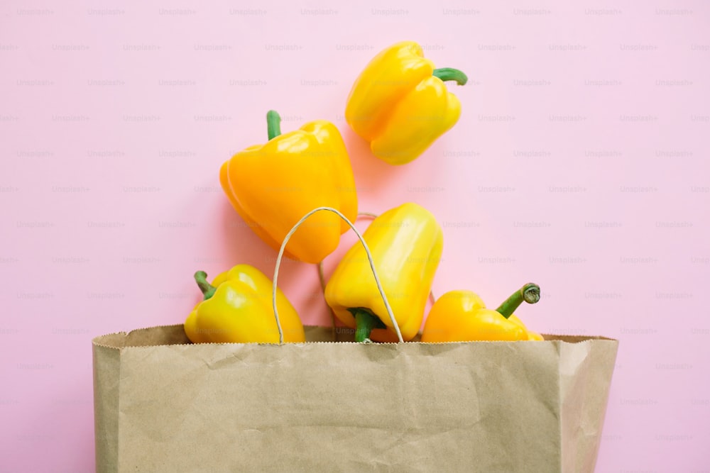 Bell peppers in paper bag on pink background flat lay. Zero waste shopping, plastic free. Shopping groceries online. Order fresh organic food and get them delivered safe. Stay home