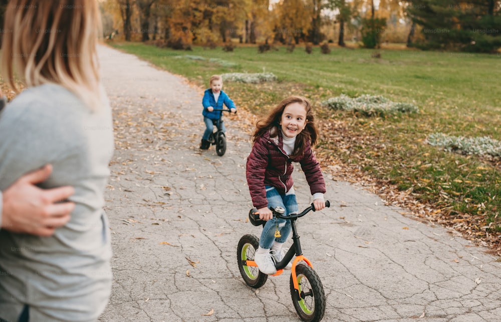 Caucasian kids riding their bikes and smiling happily to their parents during a together walk in the park