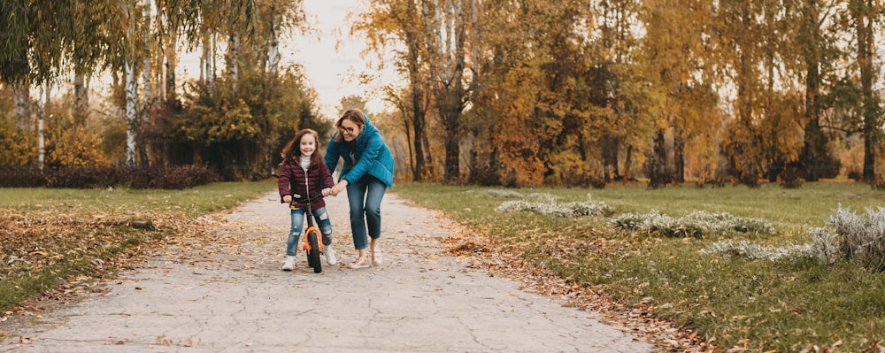 Caucasian mother with eyeglasses is teaching her small girl to ride the cycle during an autumn walk