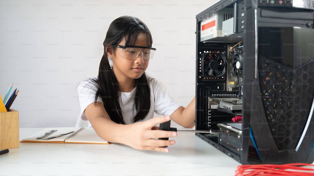 Entzückendes Schulmädchen, das lernt, eine Computerhardware zu reparieren, die einen weißen Schreibtisch mit Schraubendreher und Technikerausrüstung über einer weißen, isolierten Wand als Hintergrund aufstellt.