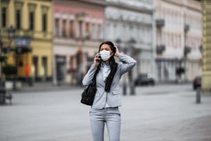 젊고 우아한 사업가는 빈 도시 거리를 걷고 위험한 독감이나 바이러스로부터 자신을 보호하기 위해 보호 마스크를 착용합니다. 코로나 바이러스 또는 Covid-19 개념.