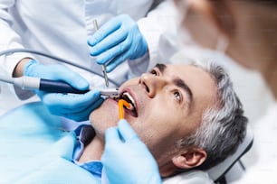 El hombre está acostado en el sillón dental y el dentista y el asistente le están haciendo una endodoncia