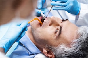 El hombre está acostado en el sillón dental y está siendo tratado por un dentista y una enfermera mientras se le administra una endodoncia