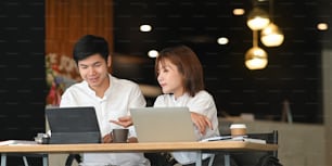 ウェブサイト管理者チームが、豪華なカフェを背景にモダンな木製のテーブルに一緒に座りながら、コンピューター、タブレット、ラップトップで作業している写真。オフィスのコンセプトの外で仕事をする。
