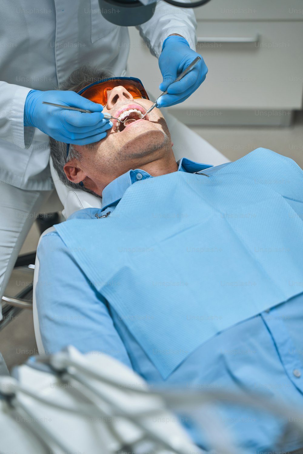 El hombre está acostado en el sillón dental y está siendo tratado por el dentista con espejo y explorador