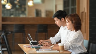 Photo of website administrator team working with computer tablet and laptop while sitting together at the modern wooden table over luxury cafe as background. Working outside the office concept.
