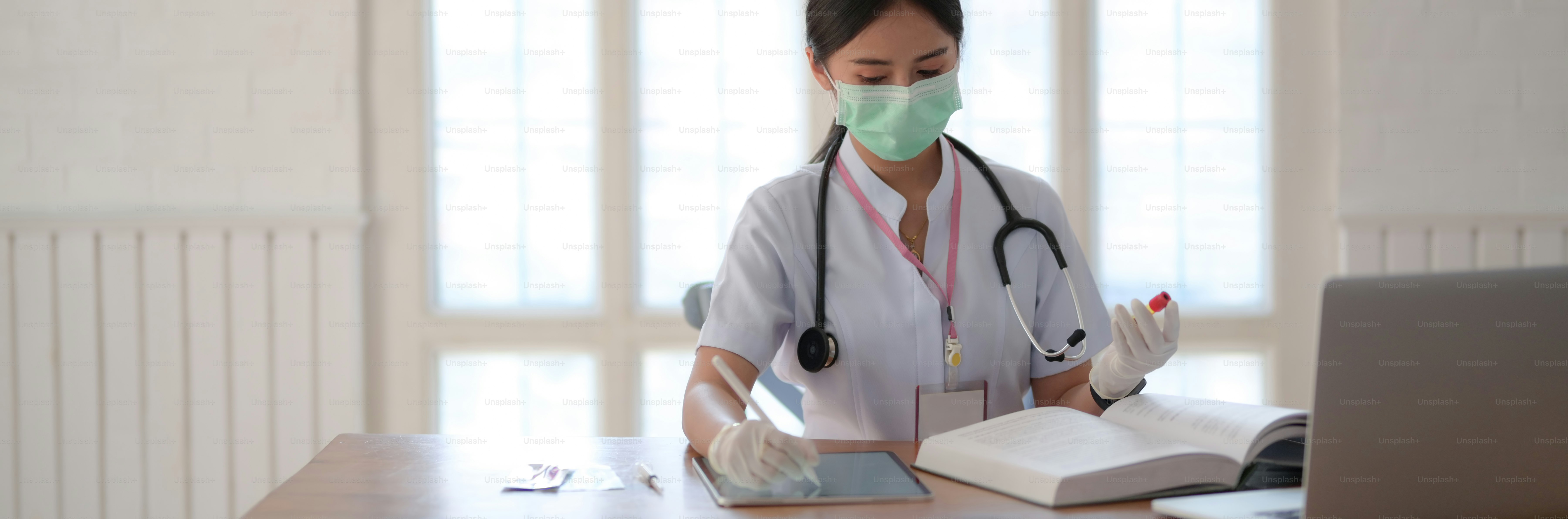 Cropped shot of female doctor holding test tube and looking for Information in a Medical Book and laptop while writing on digital tablet