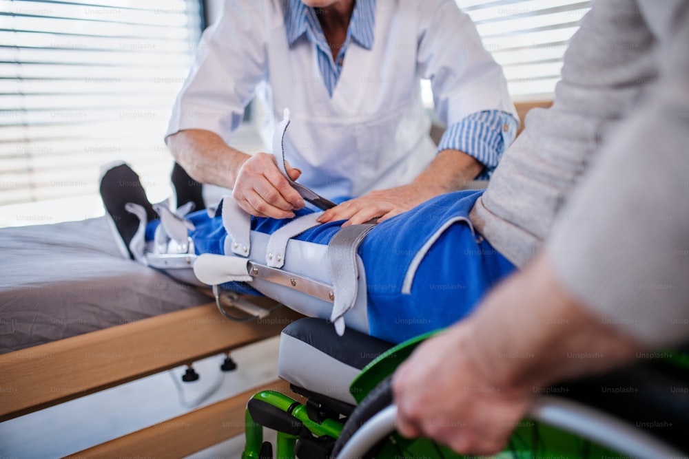 Unrecognizable healthcare worker and man paralysed senior patient in hospital, applying orthosis.