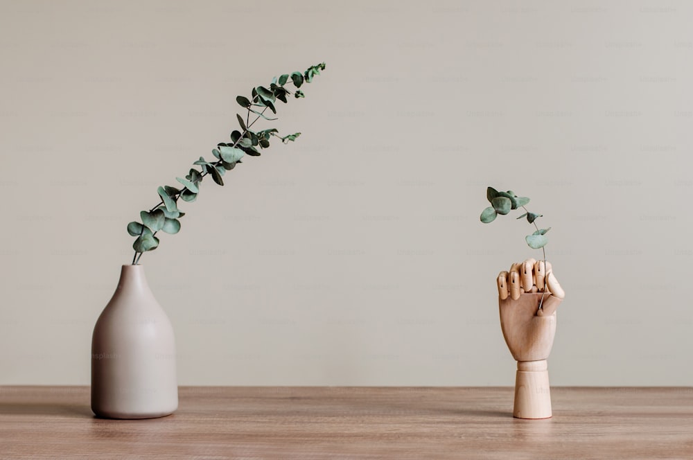Dry eucalyptus branches in modern vase and wooden hand on the wooden table indoor. Blank space for text. Modern home interior design elements background.
