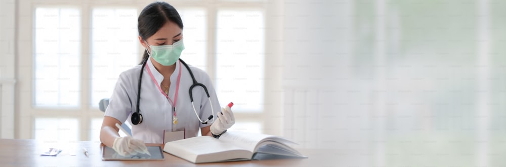 Plan recadré d’une femme médecin lisant un livre pour analyser un test sanguin alors qu’elle est assise dans une salle d’examen