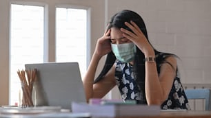 노트북을 사용하여 covid-19 바이러스 (코로나 바이러스)에 감염된 젊은 여성과 집에서 자신을 격리하면서 테이블에 앉아 있습니다. 감염된 사람들과 바이러스 개념의 확산.