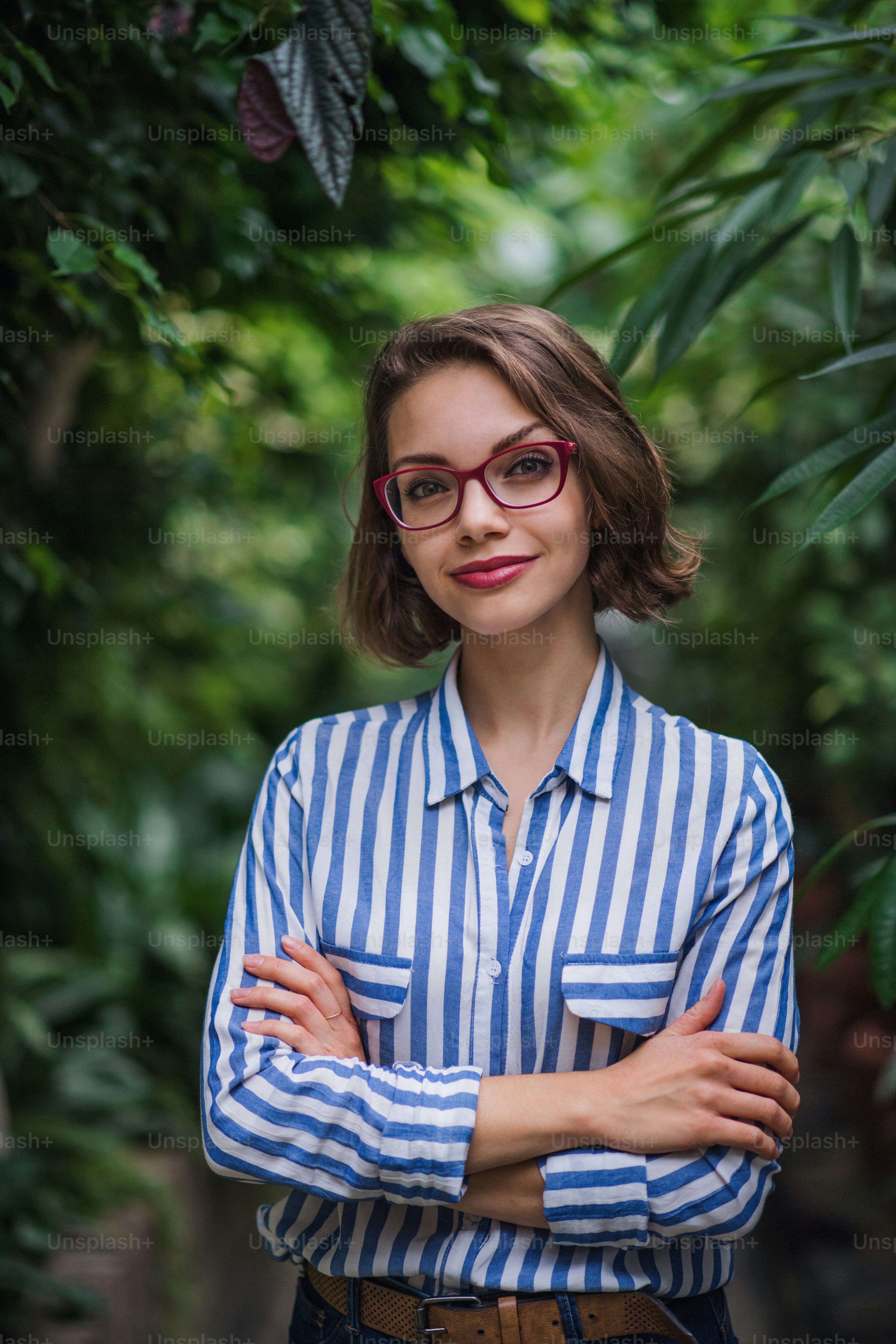 Young woman with arm crossed standing in botanical garden, looking at camera