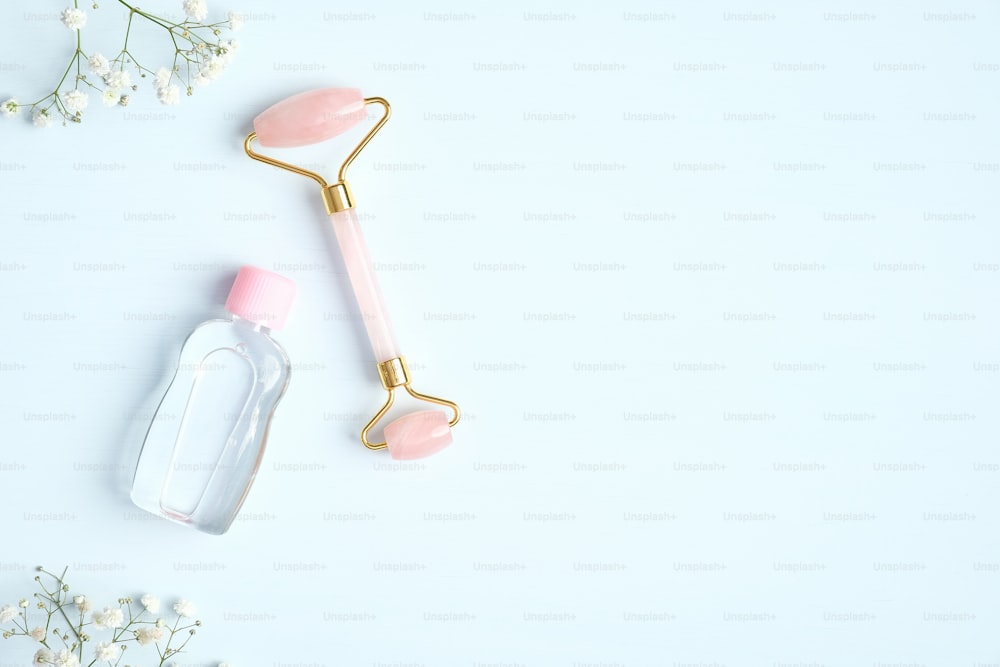 Rose quartz facial massage roller with essential oil bottle on blue background. Anti-aging, anti-wrinkle beauty skincare tool