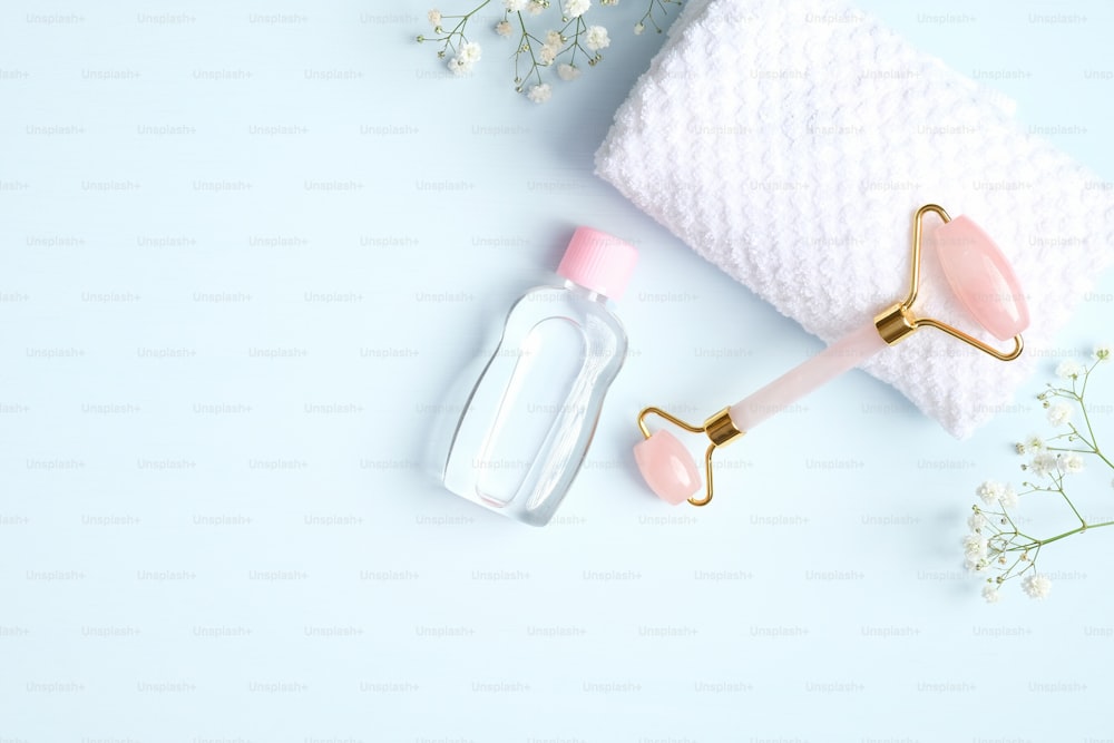 Rouleau de massage pour le visage en quartz rose avec serviette et fleurs de gypsophile sur fond bleu. Masseur facial à la pierre de jade, outil de soin de la peau de beauté anti-âge et anti-rides