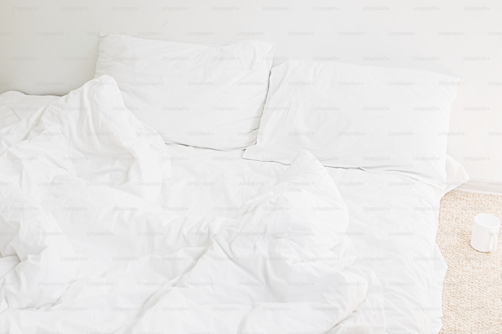 Gemütliches weißes Bett am Morgen. Weiße Bettwäsche und Kissen auf dem Bett im modernen weißen Zimmer. Faule Tage. Bleib zu Hause. Komfortabler Ort. Entspannen Sie sich am Wochenende im Hotelzimmer. Unordentliches Bett