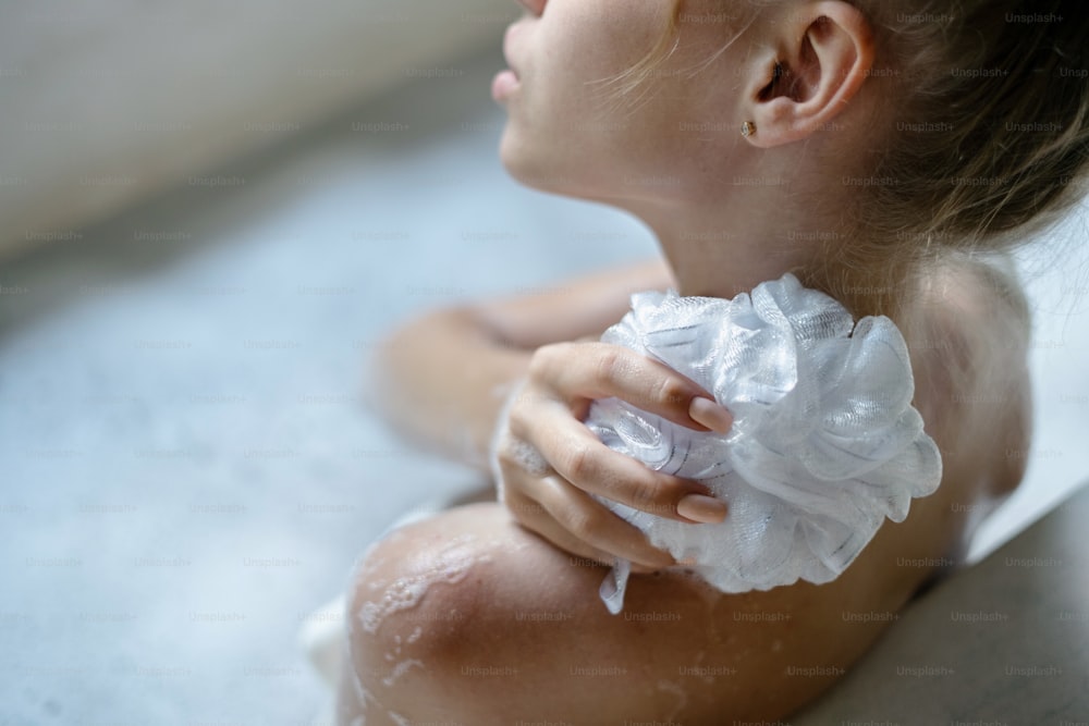 Körperpflegekonzept. Verkürzte und hohe Winkelansicht eines jungen erwachsenen Mädchens, das ein Bad nimmt, Seifenschaumwasser genießt, Schwamm in der Hand hält, zurückgespült