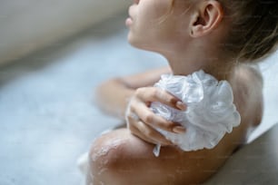 Bodycare concept. Cropped and high angle view of young adult girl taking bath, enjoying soap foam water, holding sponge in hand, washed back