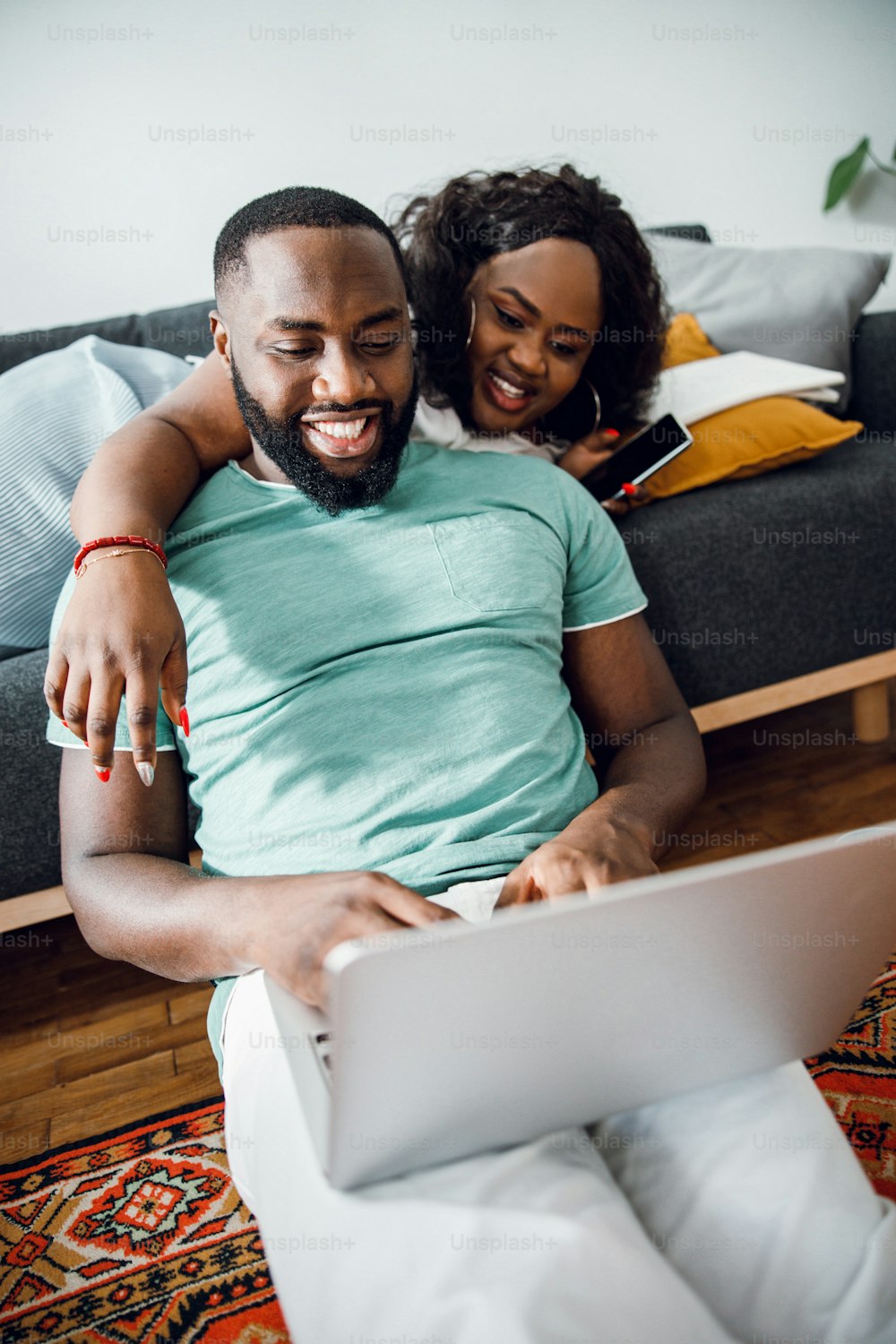 Smiling lady lying on the sofa and her boyfriend using a laptop while sitting on the floor