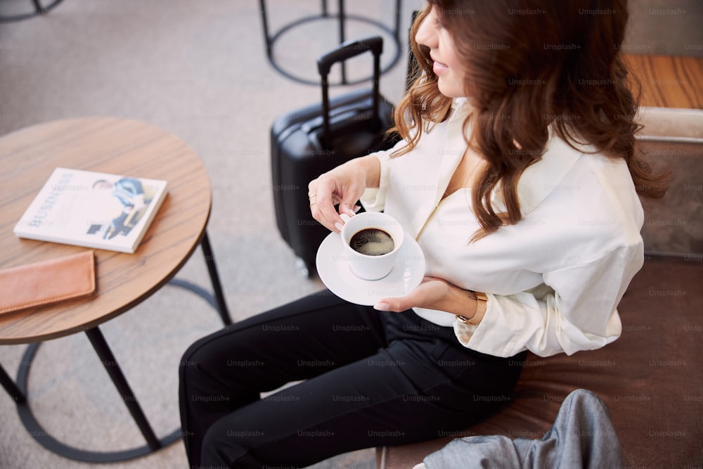 Close up of young woman holding cup of coffee while sitting at the table with book and wallet stock photo