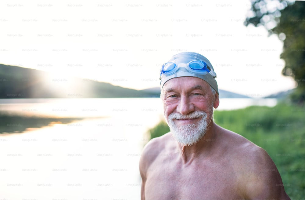 Cheerful senior man in swimsuit standing by lake outdoors before swimming.