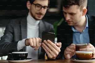 One-on-one meeting. Two young business people sitting at table in restaurant having a conversation using a phone and having a coffee