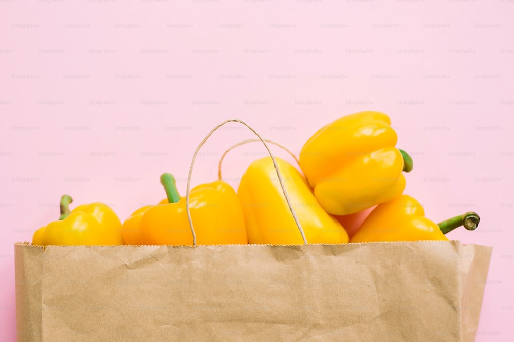 Bell peppers in paper bag on pink background flat lay. Zero waste shopping, plastic free. Shopping groceries online. Order fresh organic food and get them delivered safe. Stay home