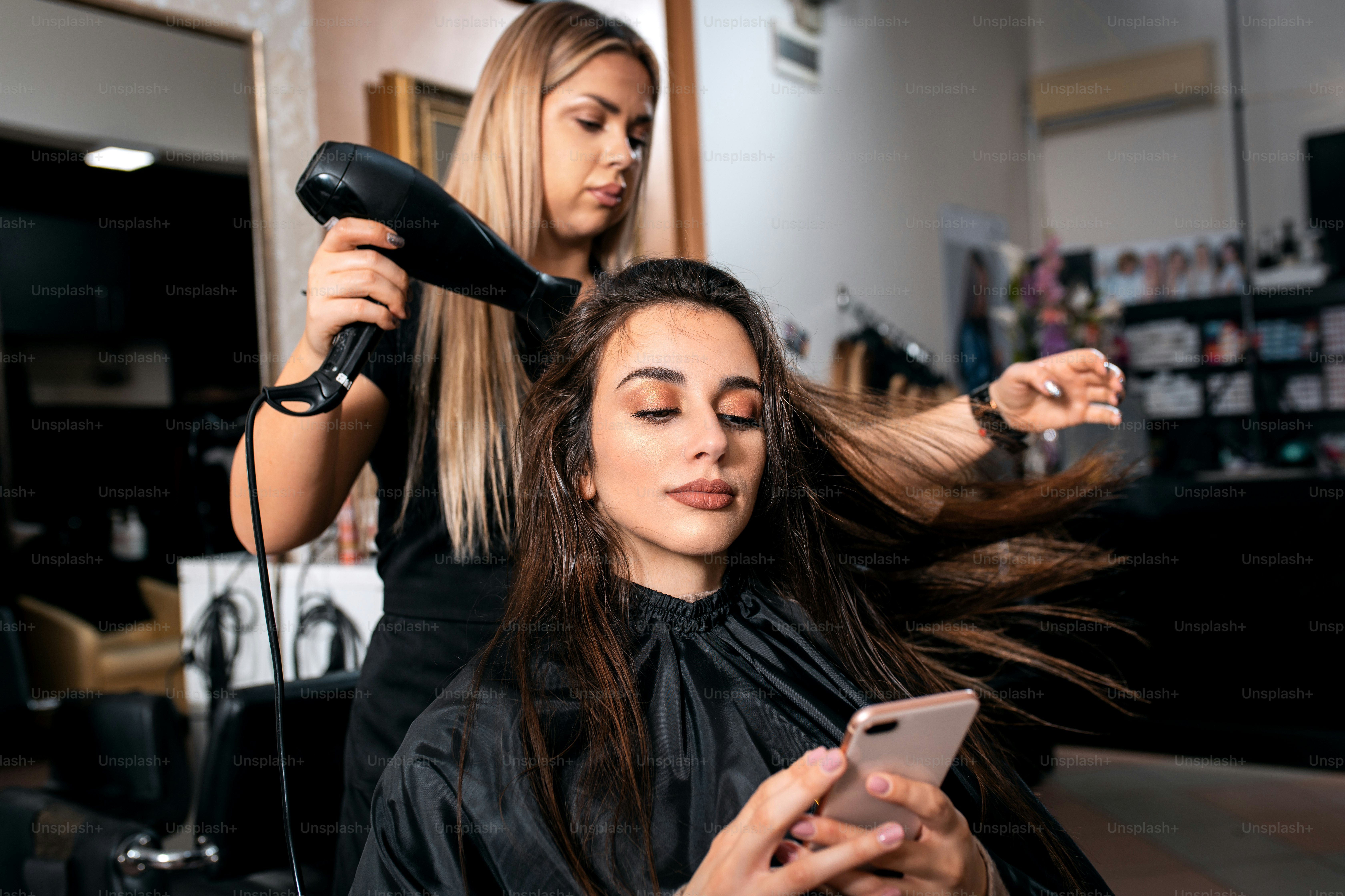 Female hairdresser makes hairstyle on young woman with brunette hair in salon.