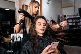 Female hairdresser makes hairstyle on young woman with brunette hair in salon.