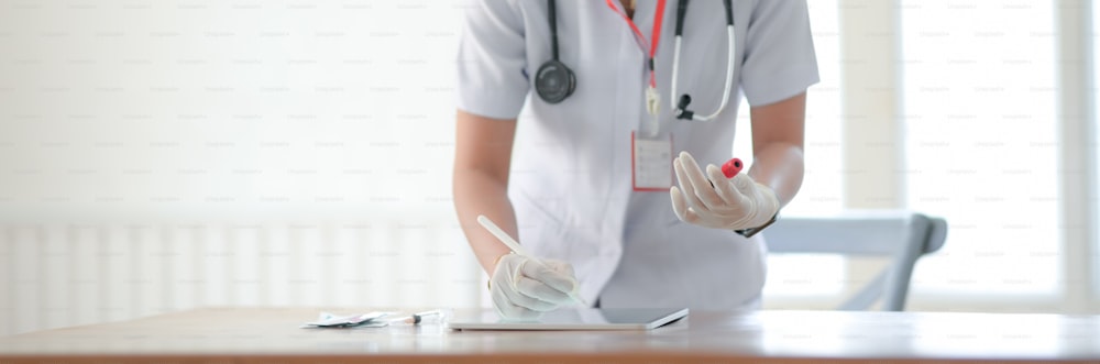 Abgeschnittene Aufnahme einer Ärztin, die Bluttests auf einem digitalen Tablet schreibt, während sie im Untersuchungsraum steht
