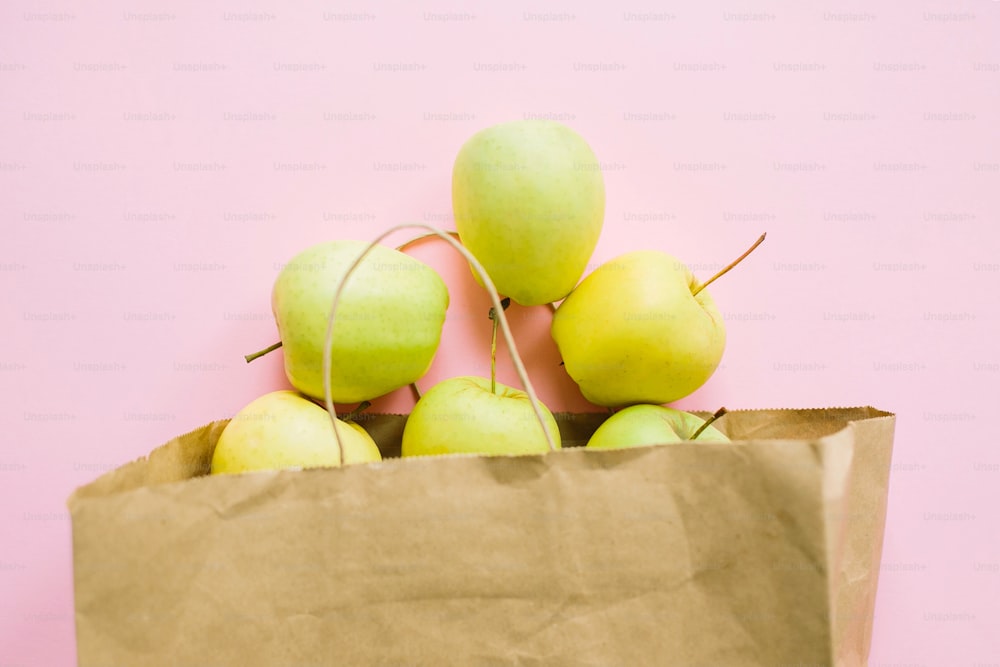 분홍색 배경에 종이 봉지에 사과가 놓여 있습니다. 제로 폐기물 쇼핑, 플라스틱 무료. 식료품 온라인 쇼핑. 신선한 유기농 식품을 주문하고 안전하게 배달하십시오. 집에 머물러 라.
