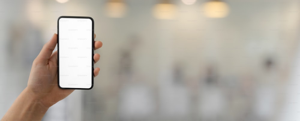 Cropped shot of a man holding blank screen smartphone in blurred glass wall office room background