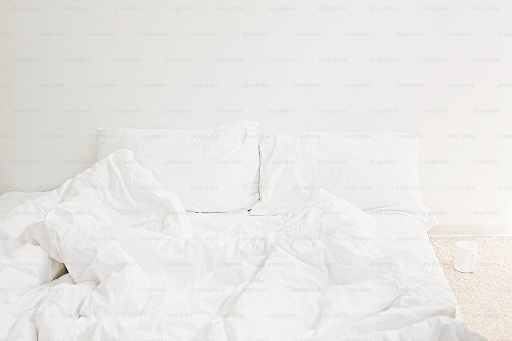 아침에 아늑한 흰색 침대. 현대적인 화이트 룸의 침대에 화이트 시트와 베개. 게으른 날. 집에 계세요. 편안한 장소. 주말에는 호텔 객실에서 휴식을 취하십시오. 지저분한 침대