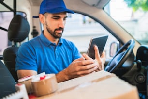 Portrait of a delivery man driver using digital tablet while sitting in van. Delivery service and shipping concept.