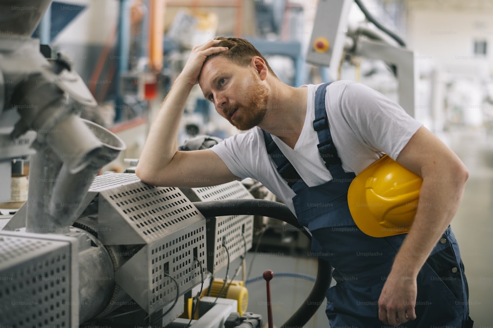 Factory worker having problem with production line. Factory. Engineer. Manual worker. Manufacturing. Production. Wearing protective clothes. Yellow helmet.