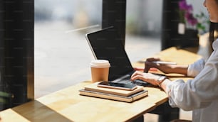 Photo of gorgeous woman in white shirt working with stylus pen and computer tablet while sitting at the wooden counter bar over modern cafe/restaurant as background.