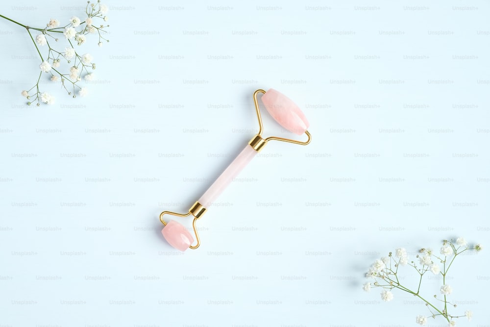 Rose quartz facial massage roller on blue background with gypsophila flowers. Facial massager with jade stone, anti-aging, anti-wrinkle beauty skincare tool