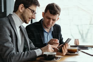 One-on-one meeting. Two young business people sitting at table in restaurant having a conversation using a phone and having a coffee
