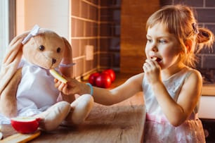 Petite fille jouant avec une peluche de lapin en le nourrissant avec une tranche de pomme fraîche dans la cuisine. Mise au point sélective.