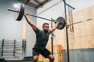 Retrato de un joven atleta de gimnasio haciendo ejercicio con una barra. Concepto de gimnasio, deporte y estilo de vida saludable.