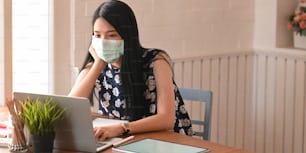 Mujer joven que infectó un virus covid-19 (virus corona) usando una computadora portátil y sentada en la mesa mientras mantenía una cuarentena en casa. Personas infectadas y propagación del concepto de virus.