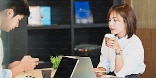 Photo of young couple working with computer laptop and computer tablet while sitting together at the working table over modern and comfortable living room as background.