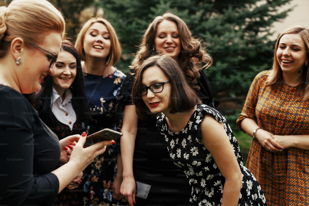 stylish elegant women holding and showing phone screen at celebration sunny in park, funny moment