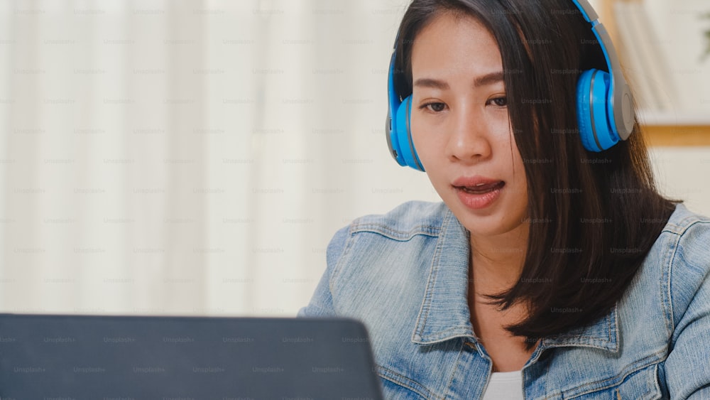 Freelance business women casual wear using laptop working call video conference with customer in workplace in living room at home. Happy young Asian girl relax sitting on desk do job in internet.